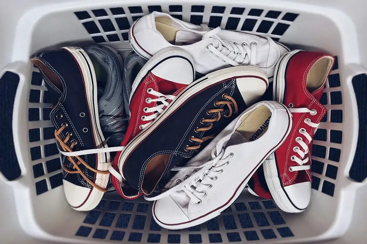 Kosz z butami Converse, gotowymi do prania w pralce. Białe, czerwone i czarne trampki czekają na odświeżenie.