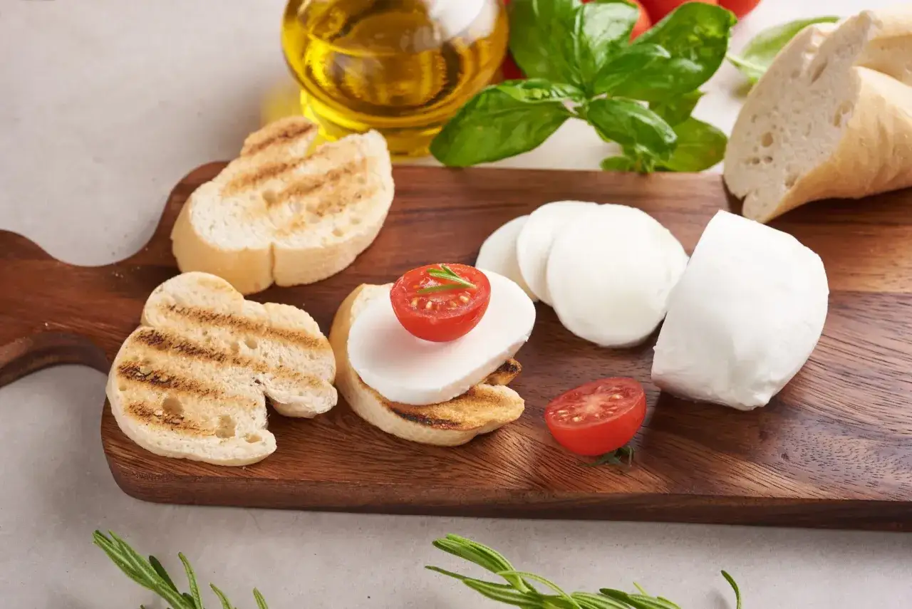 Na desce drewnianej grzanki z mozzarellą i pomidorkami. Czy mozzarella ma dużo białka? Tak, to świetne źródło białka!