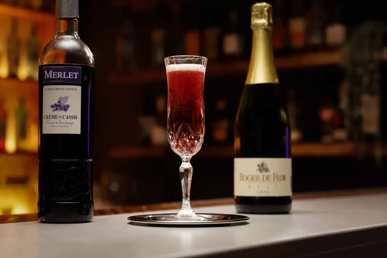 Kieliszek musującego Kir Royale, obok butelki crème de cassis i szampana.