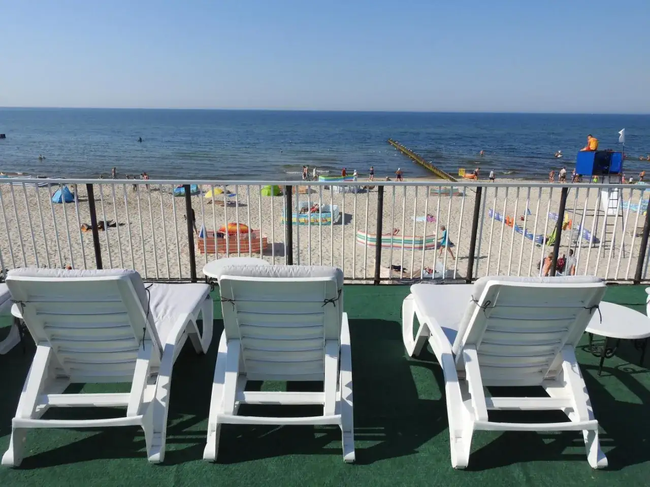 Idealne noclegi przy plaży z widokiem na morze. Białe leżaki czekają na gości, by mogli podziwiać błękitne morze i piaszczystą plażę.