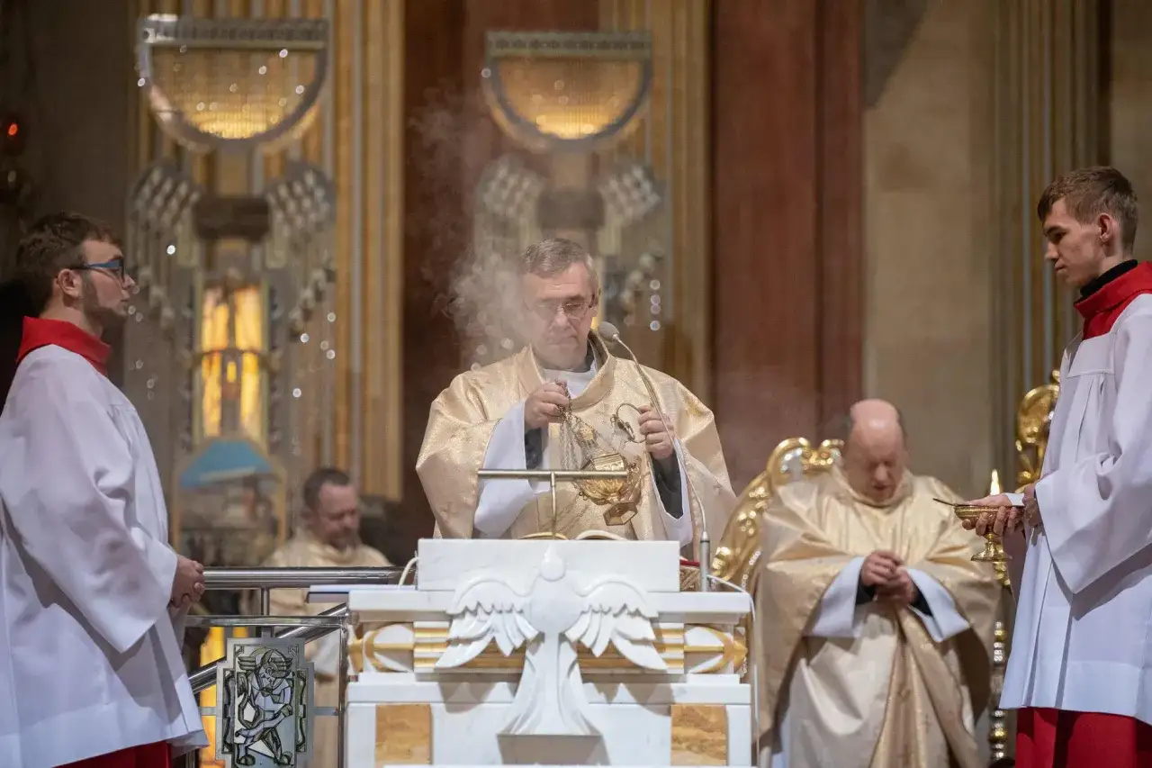 Uroczysta liturgia Wielkiego Czwartku. Kapłan okadza ołtarz, towarzyszą mu ministranci w białych albach.