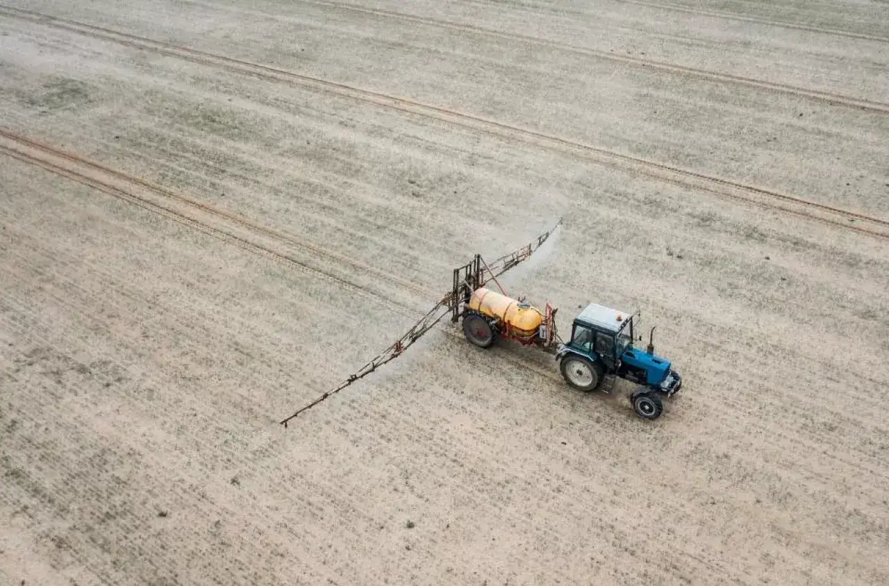 Traktor opryskuje pole, rozprowadzając środek chwastobójczy. To pokazuje, jak działa glifosat, co to jest i jak jest stosowany w rolnictwie.