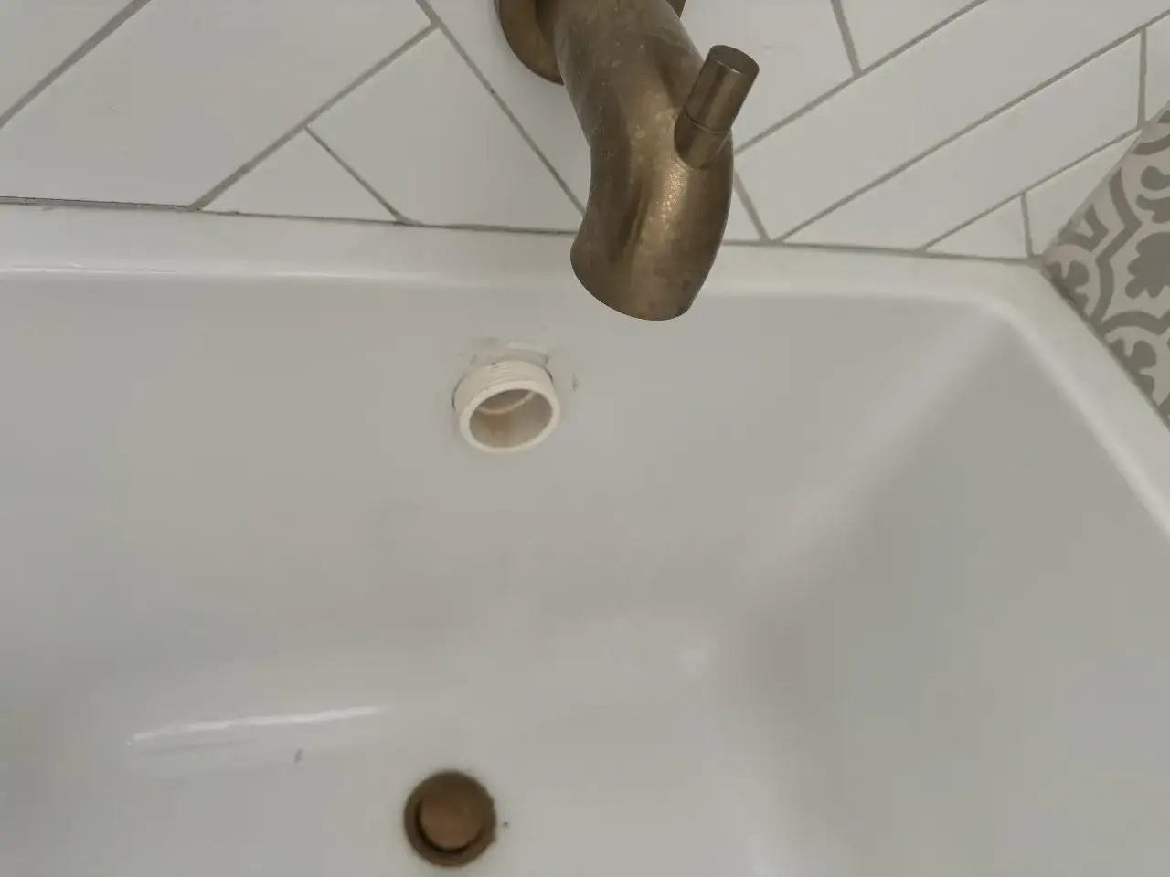 Biała wanna z widocznym elementem do podłączenia wanny do odpływu. Nad wanną złota bateria.