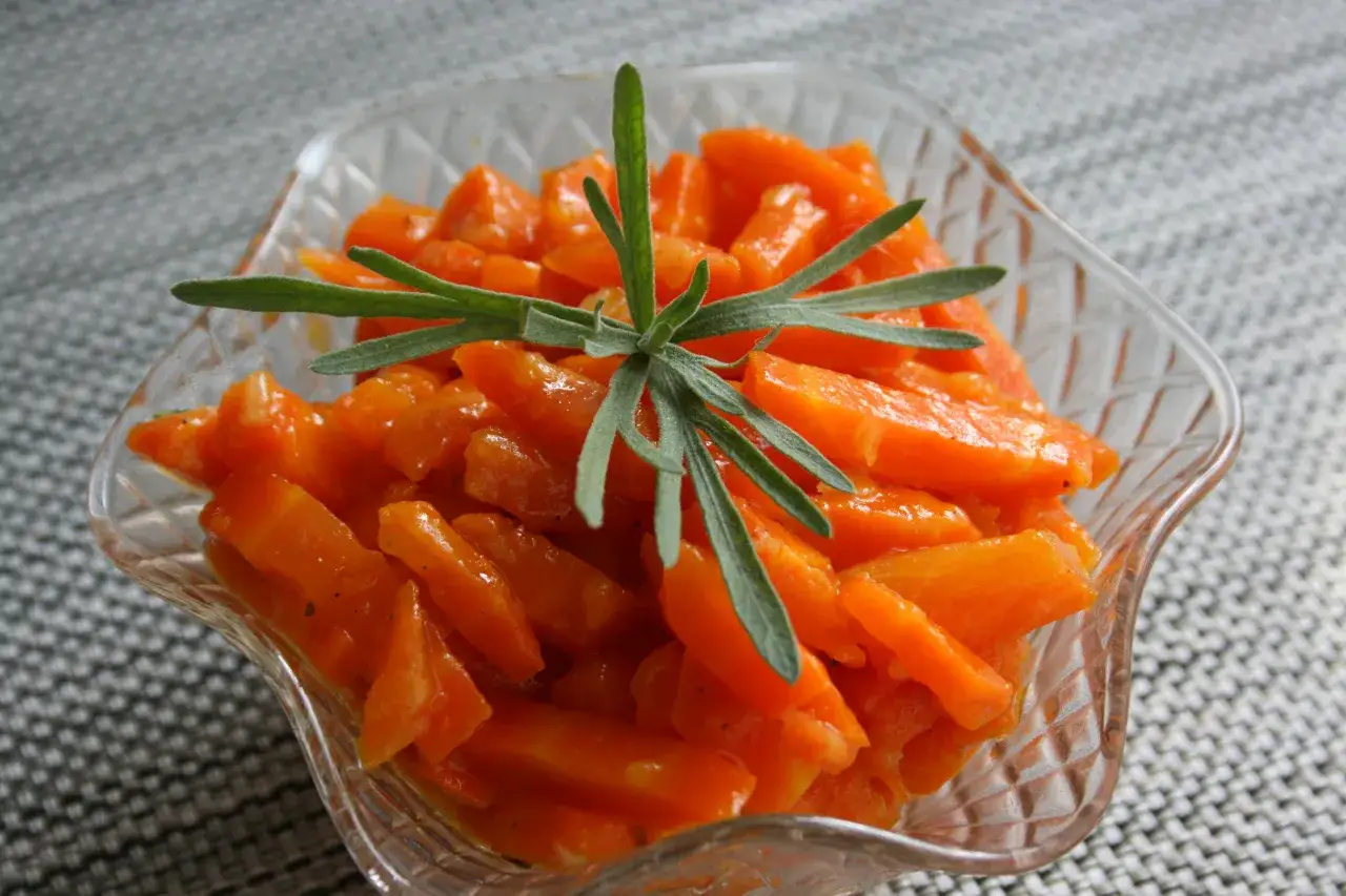 Ciepła, aromatyczna marchewka do obiadu, podana w szklanej miseczce, ozdobiona gałązką ziół.