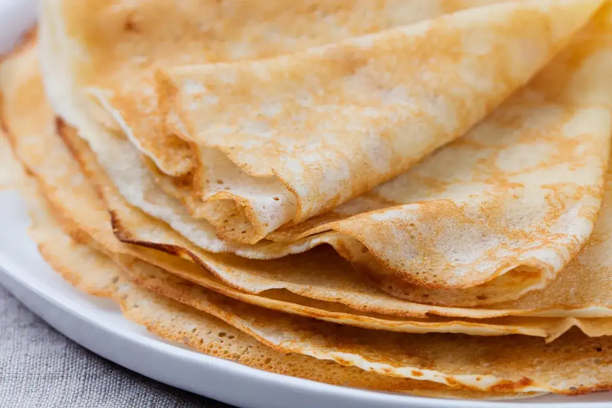 Stos naleśników na białym talerzu. Dowiedz się, dlaczego naleśniki przyklejają się do patelni, by cieszyć się idealnym śniadaniem.
