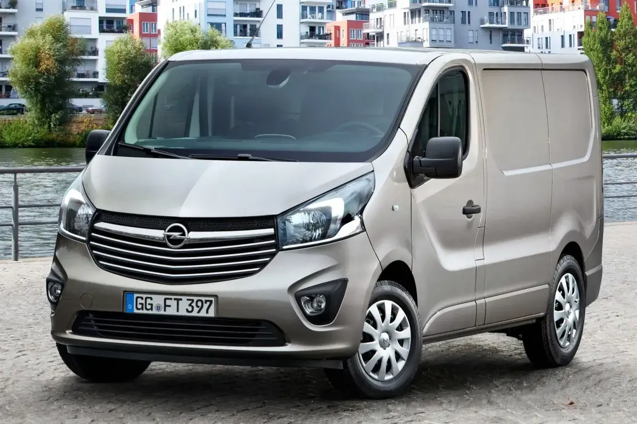 Brązowy Opel Vivaro, idealny do pracy i podróży, z niskim opel vivaro spalanie. W tle nowoczesne budynki nad rzeką.