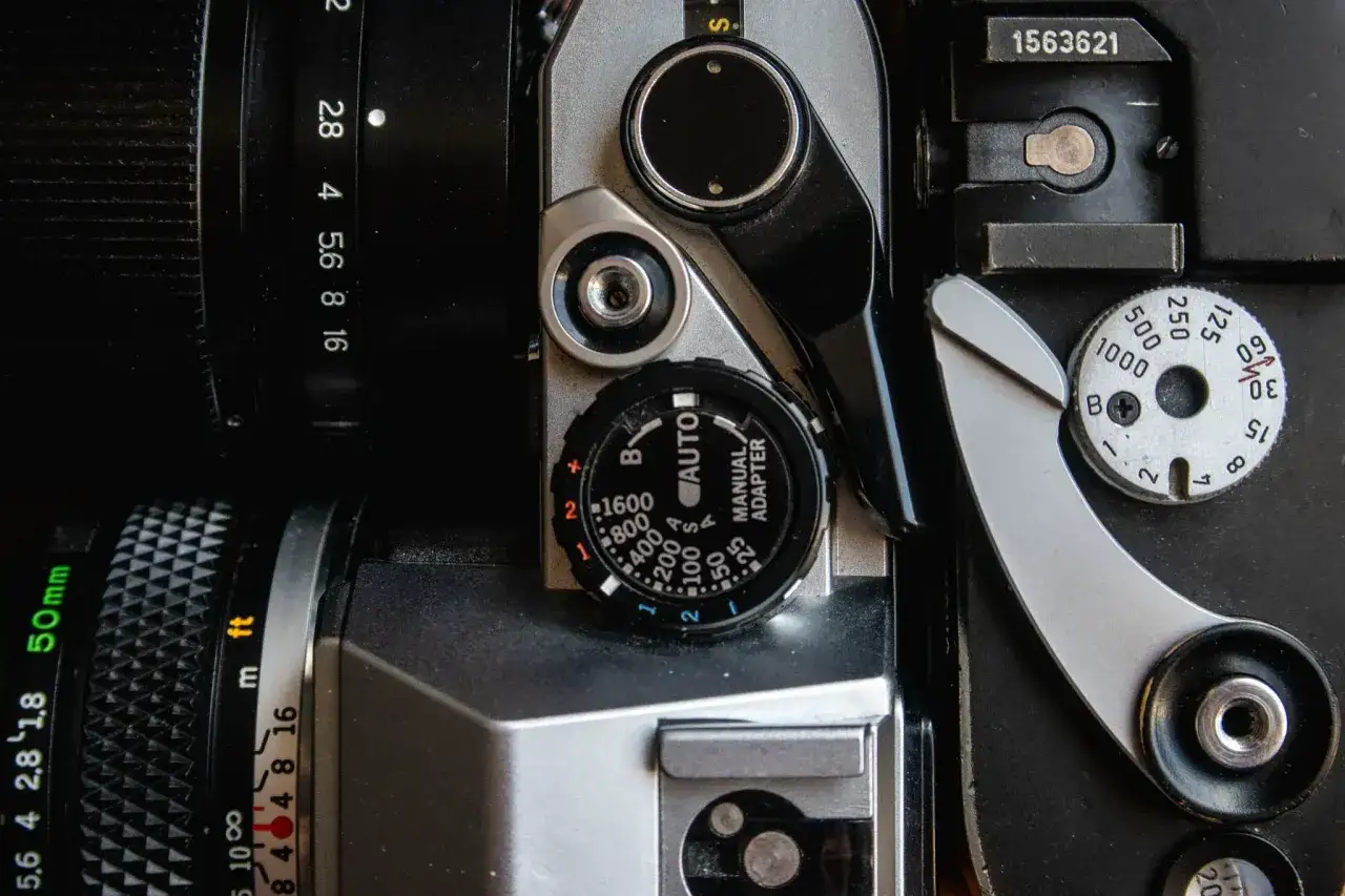 Zbliżenie na aparat analogowy, widoczne pokrętła ustawień, obiektyw 50mm i oznaczenia przysłony. Jaka klisza do aparatu?