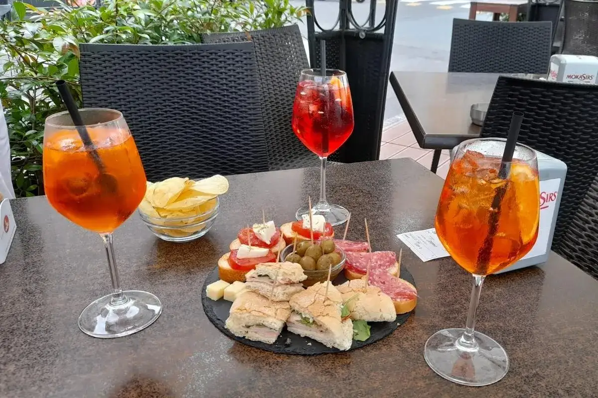 Aperol Spritz z czym? Na stole Aperol, chipsy, oliwki, kanapki i bruschetta. Idealne prosecco z przekąskami.