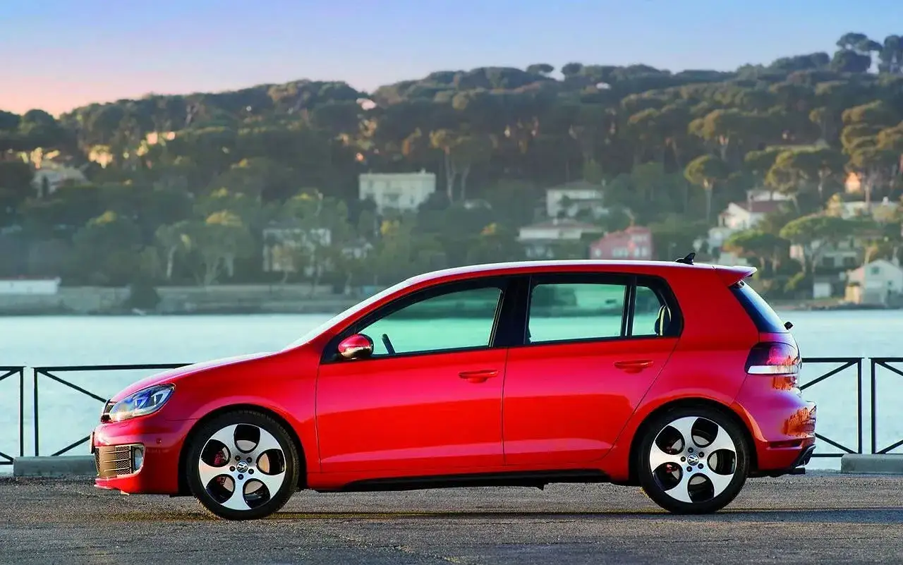 Czerwony Golf 6 R z charakterystycznymi felgami stoi nad jeziorem, w tle malownicze wzgórza z domkami.