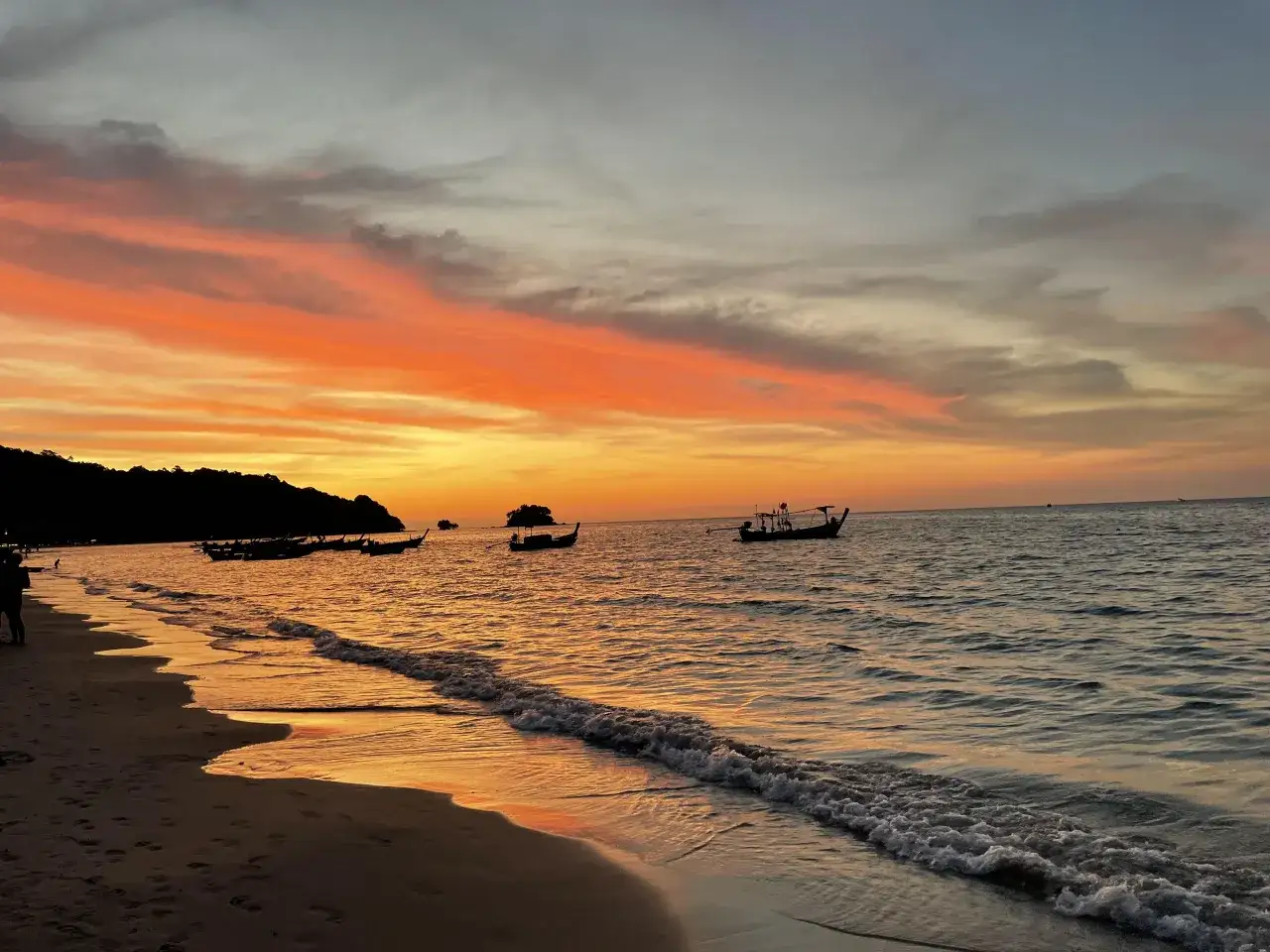 Zachód słońca na plaży, łodzie na morzu. Idealny czas, by pomyśleć, kiedy jechać na Phuket.