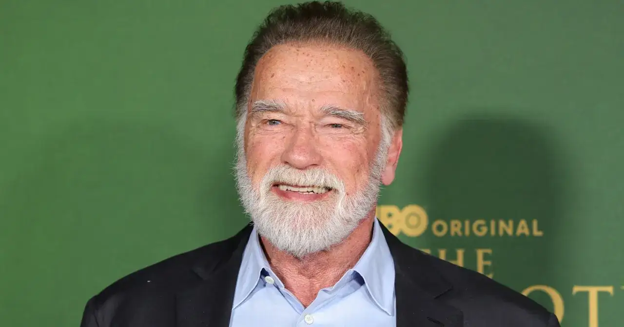 Arnold Schwarzenegger z siwą brodą i uśmiechem. W tle zielone logo HBO. Ciekawe, ile lat ma Arnold Schwarzenegger?