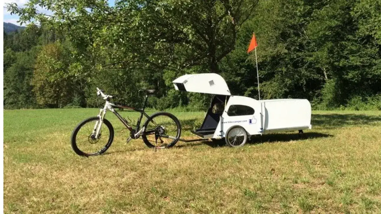 Rowerowa przyczepa kempingowa gotowa na przygodę. Biała, aerodynamiczna, z miejscem na nocleg i bagaż.