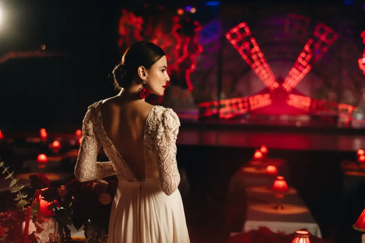 Elegancka kobieta w białej sukni z koronkowymi rękawami, inspiracja Moulin Rouge. Jak się ubrać na wieczór pełen magii i czerwonych świateł.