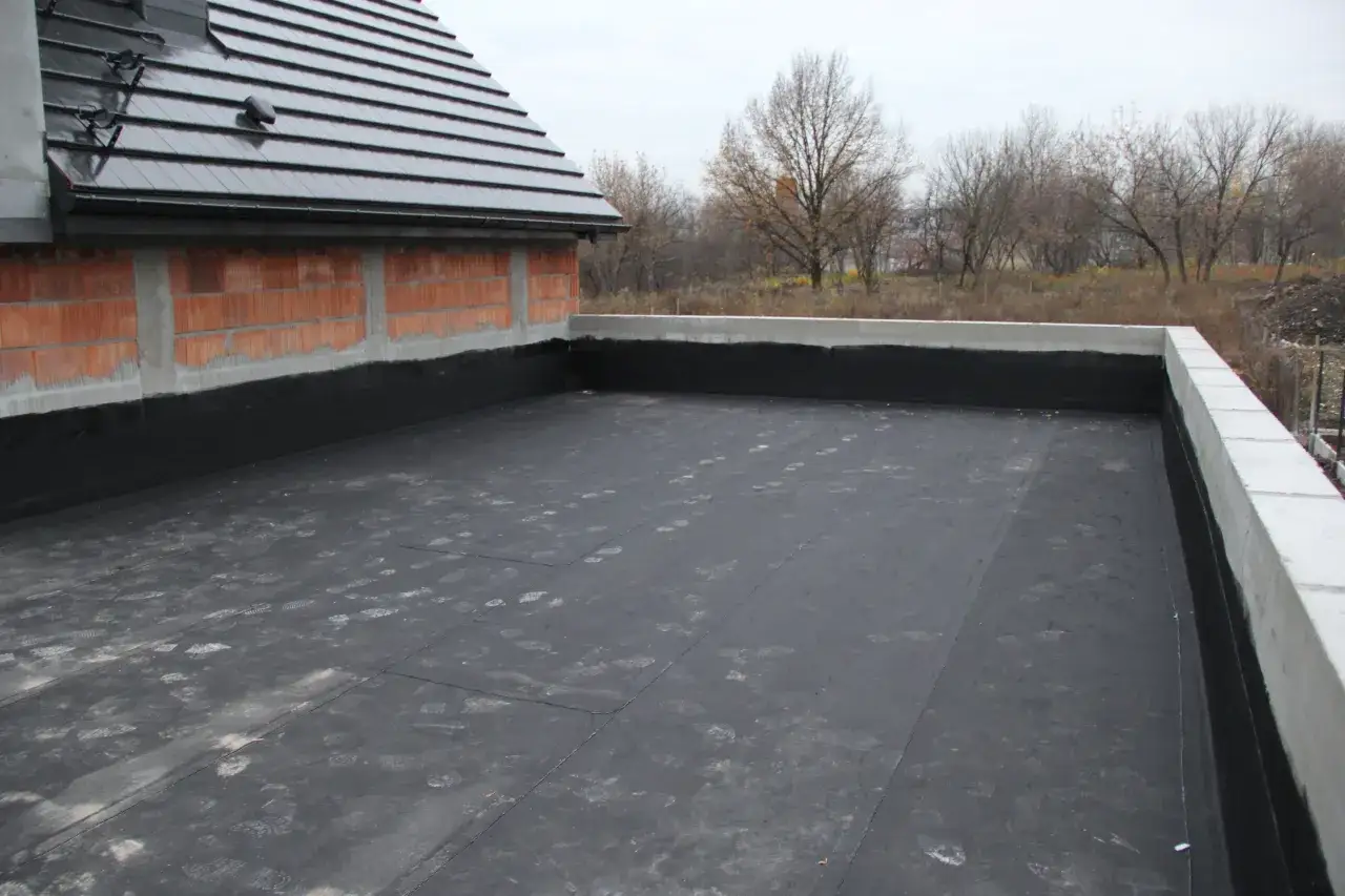 Budowa dachu płaskiego, pokrytego papą. Czy płaski dach jest tańszy? Na zdjęciu widać fragment budowy, z widocznym dachem płaskim i częścią dachu skośnego.