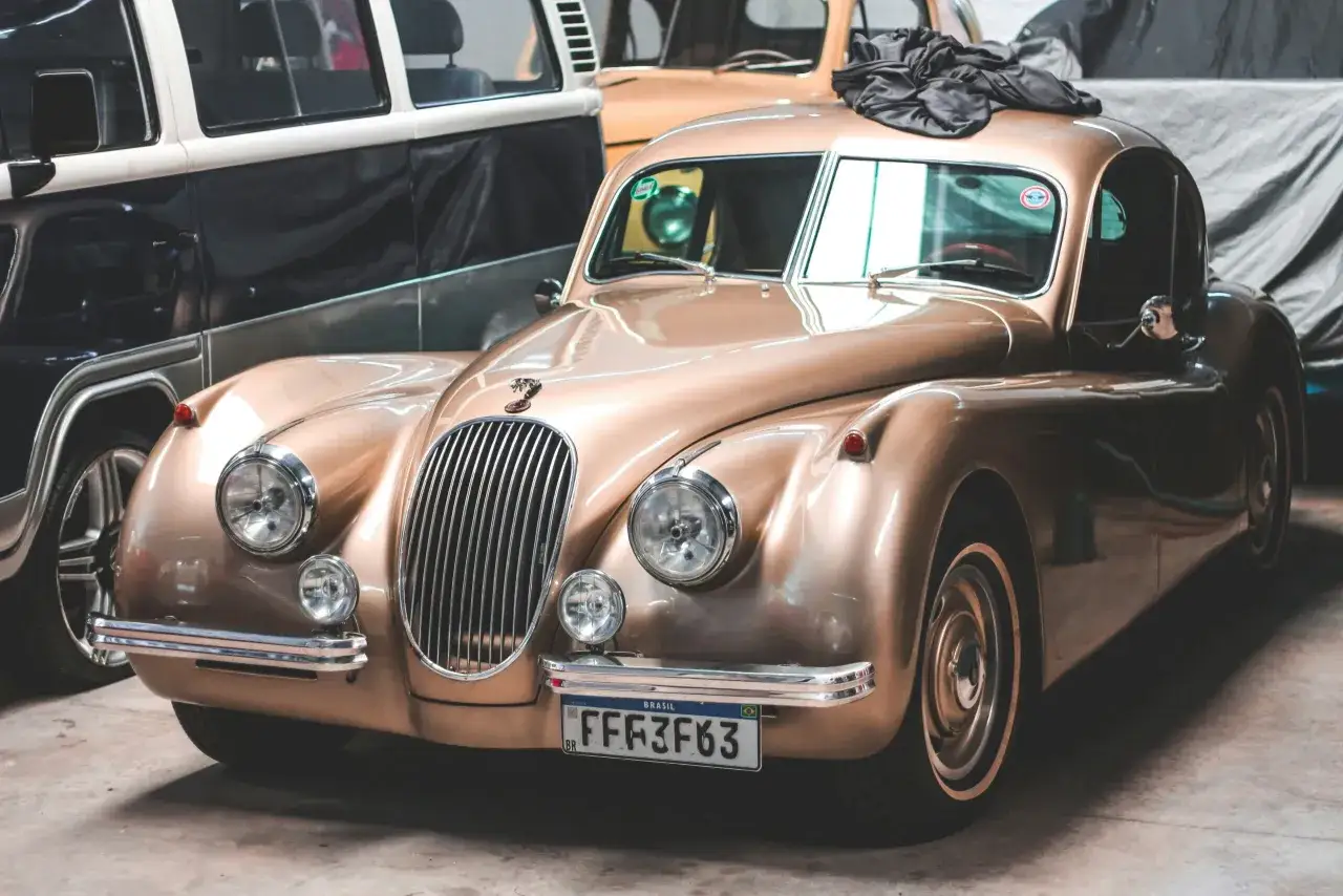 Złoty klasyczny samoch&oacute;d z chromowanymi detalami i czarną narzutą na dachu. Obok stoi czarno-biały van. To piękne zdjęcia z samochodem.