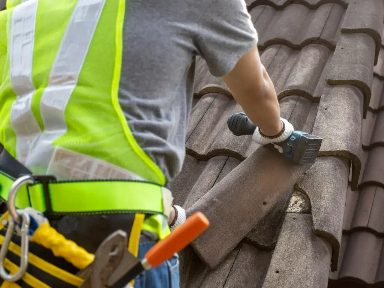 Pracownik w kamizelce odblaskowej usuwa dachówkę eternitową. Dowiedz się, ile kosztuje demontaż eternitu.