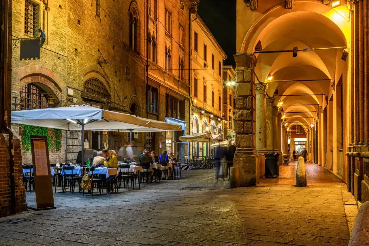 Wieczorny spacer po Bolonii, gdzie zjesc? Urokliwe arkady i stoliki restauracyjne na brukowanym placu zapraszają do kolacji.