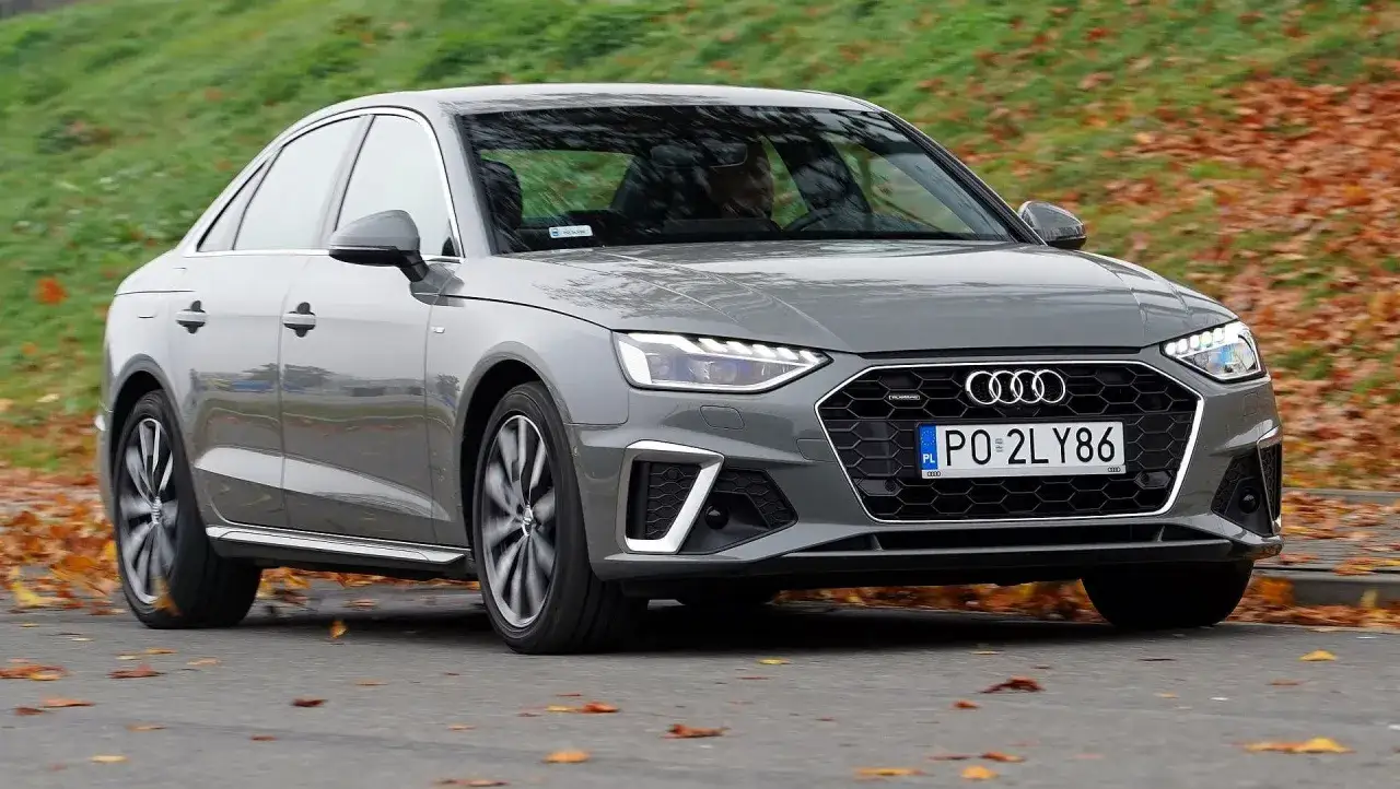 Szary Audi A4 w ruchu, jesienne liście na drodze. Pojemność baku tego modelu jest optymalna na długie podróże.