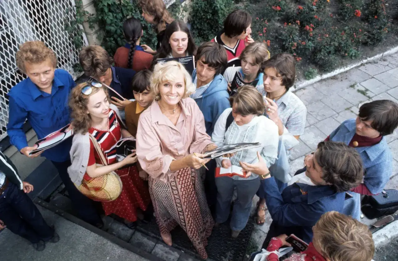 Helena Vondráčková rozdaje autografy młodym fanom. Wśród nich widać jej dzieci, które z dumą obserwują mamę.