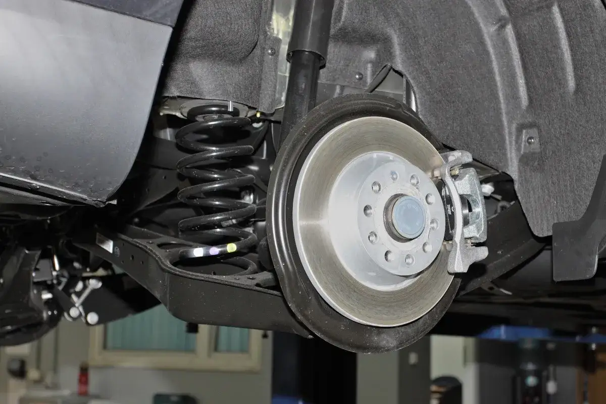 Widok tylnego zawieszenia samochodu z tarczą hamulcową i sprężyną. Pęknięta sprężyna objawy mogą być widoczne jako nier&oacute;wnomierne ugięcie nadwozia.