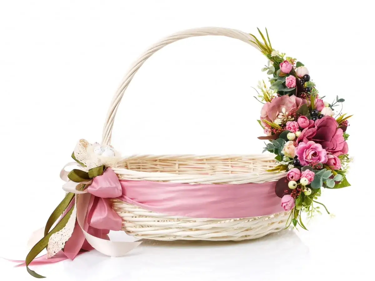 Ozdobiony kwiatami i różową wstążką koszyczek wielkanocny. Wstążka pięknie oplata koszyk, pokazując, jak ozdobić koszyczek wielkanocny wstążką.