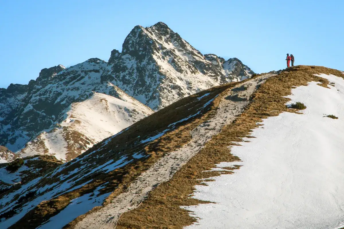 Dwaj turyści na szlaku wiodącym na przełęcz pod Kopą Kondracką. Góry pokryte śniegiem i trawą.