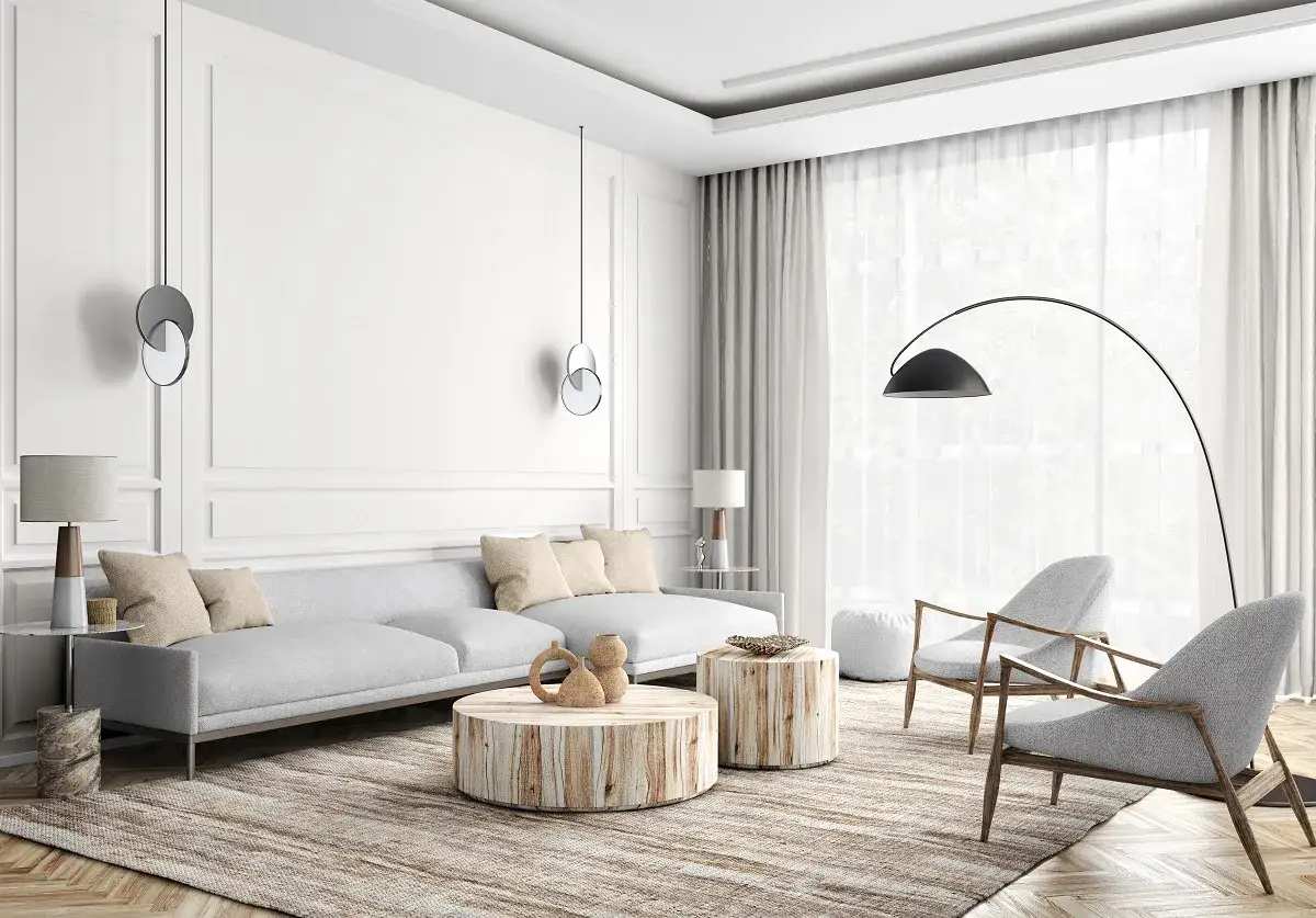 Jasny salon w stylu modern classic z szarą kanapą, drewnianymi stolikami i dwoma fotelami.