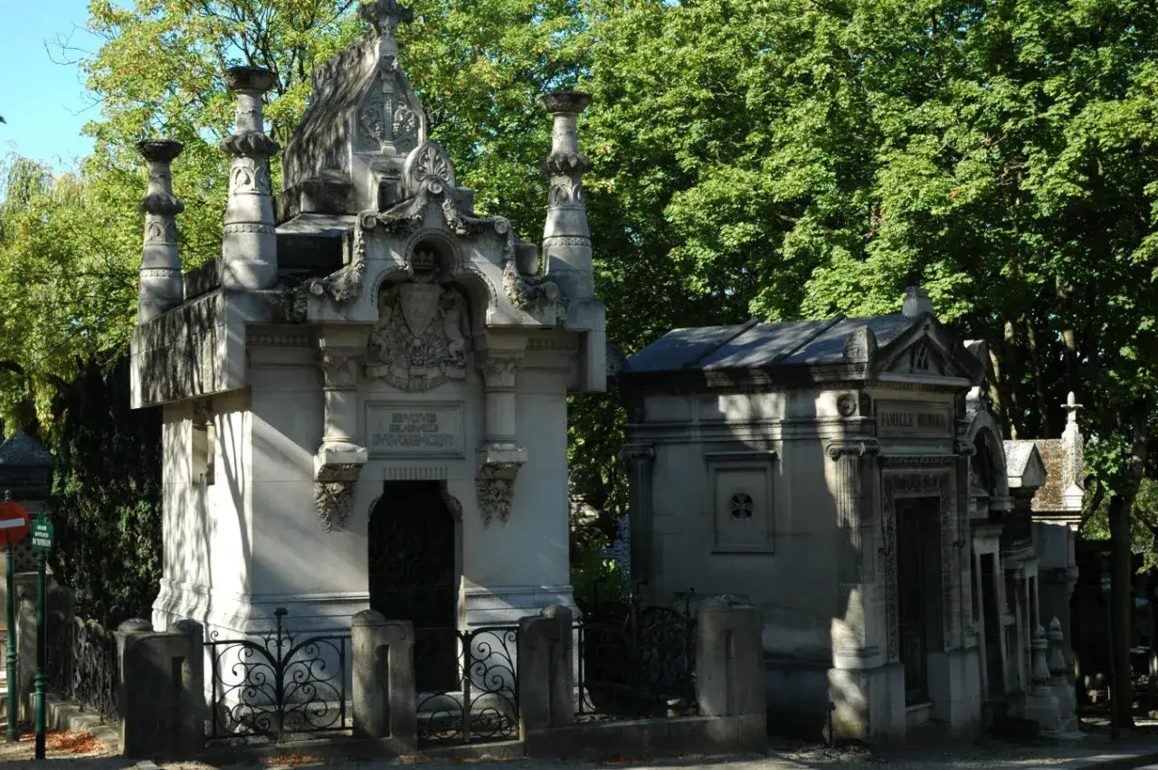 Kamienne mauzolea na cmentarzu w Paryżu, ozdobione detalami i otoczone zielenią.