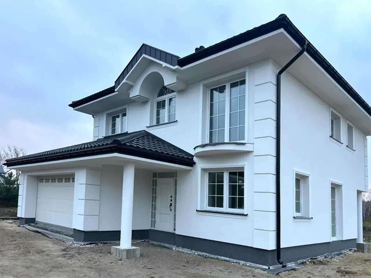 Nowoczesny dom z białym tynkiem i eleganckimi boniami listwami elewacyjnymi. Czarny dach i okna dodają mu charakteru.