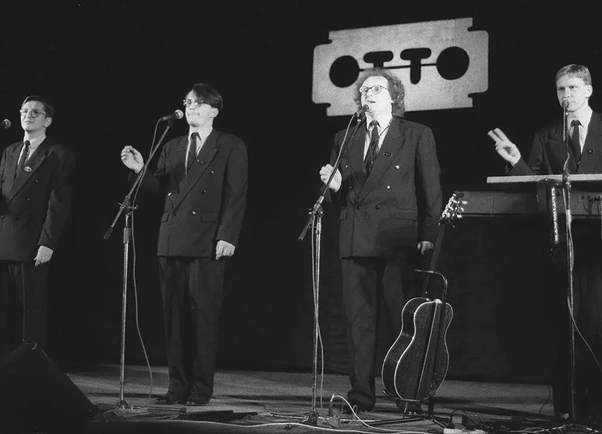 Czterech pan&oacute;w w garniturach na scenie, śpiewających do mikrofon&oacute;w. To kabaret, a w tle logo z żyletką i napisem 