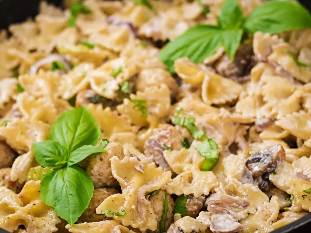 Pyszne farfalle w kremowym sosie z kurczakiem i pieczarkami, idealne na obiad w poniedziałek. Udekorowane świeżą bazylią.