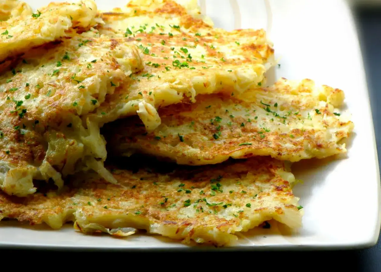 Złociste placki z kapusty kiszonej, posypane natką pietruszki, kuszą apetycznym wyglądem.