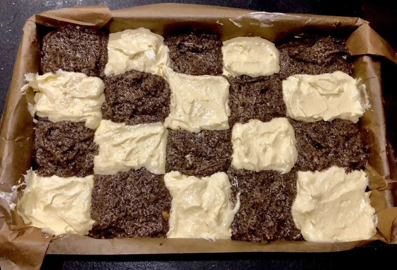 Przygotowania do pieczenia ciasta z serem i makiem. Warstwy ciasta makowego przeplatane kremem serowym w blasze wyłożonej papierem.