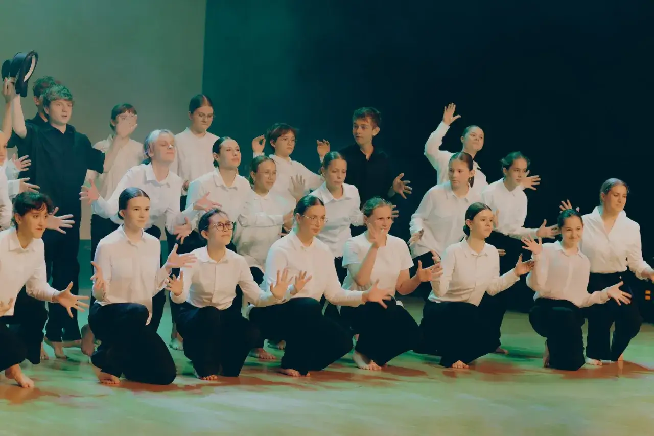 Młodzi artyści na scenie, ćwiczący swoje ruchy. W tle widać fragmenty szkół musicalowych w Warszawie.