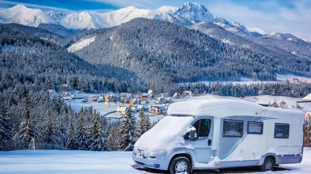 Kamper w śnieżnej scenerii górskiej wioski. Idealne wakacje kamperem zimą, otoczone ośnieżonymi drzewami i majestatycznymi szczytami.