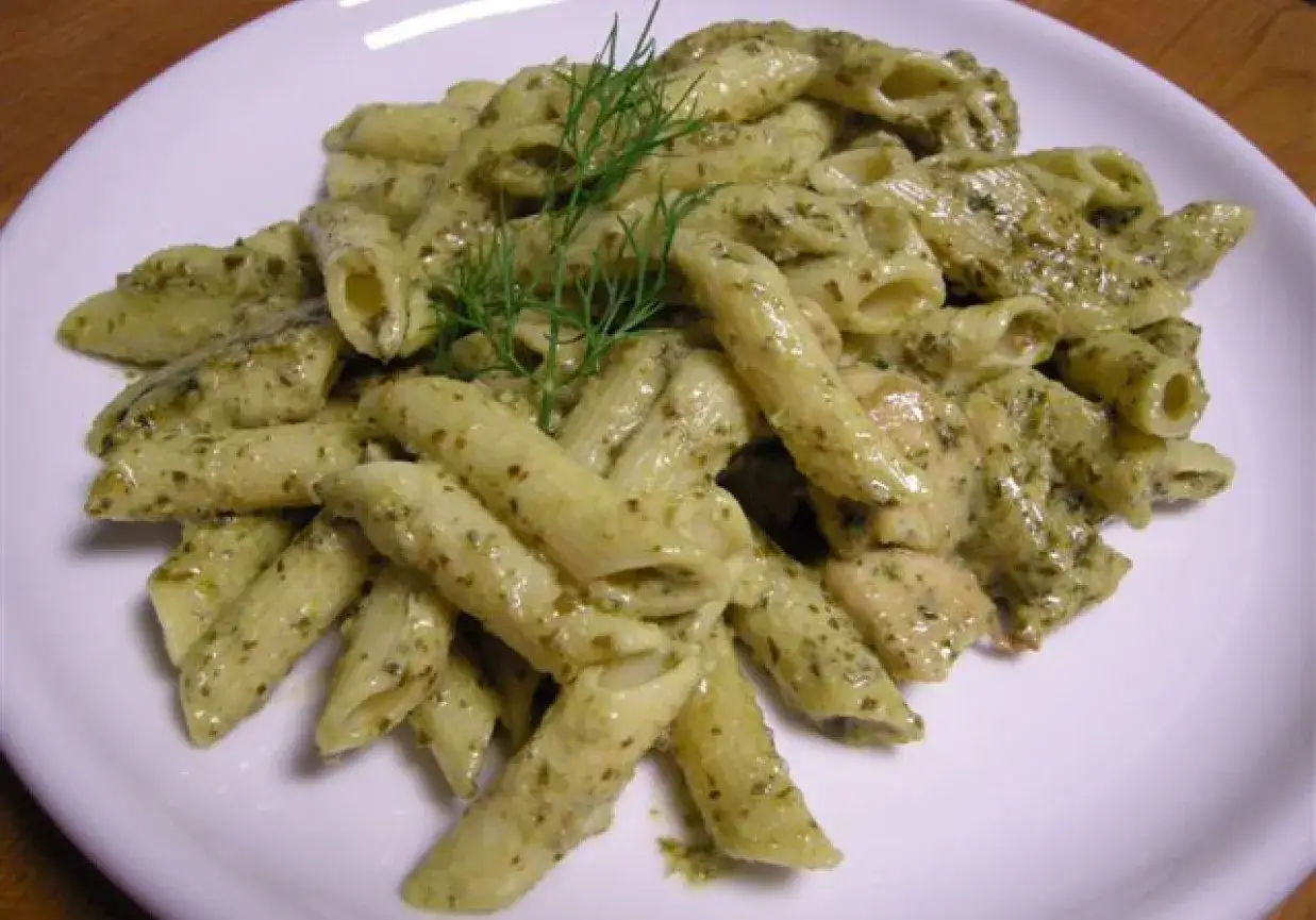 Penne z domowym pesto, śmietaną i kawałkami kurczaka, udekorowane gałązką koperku.