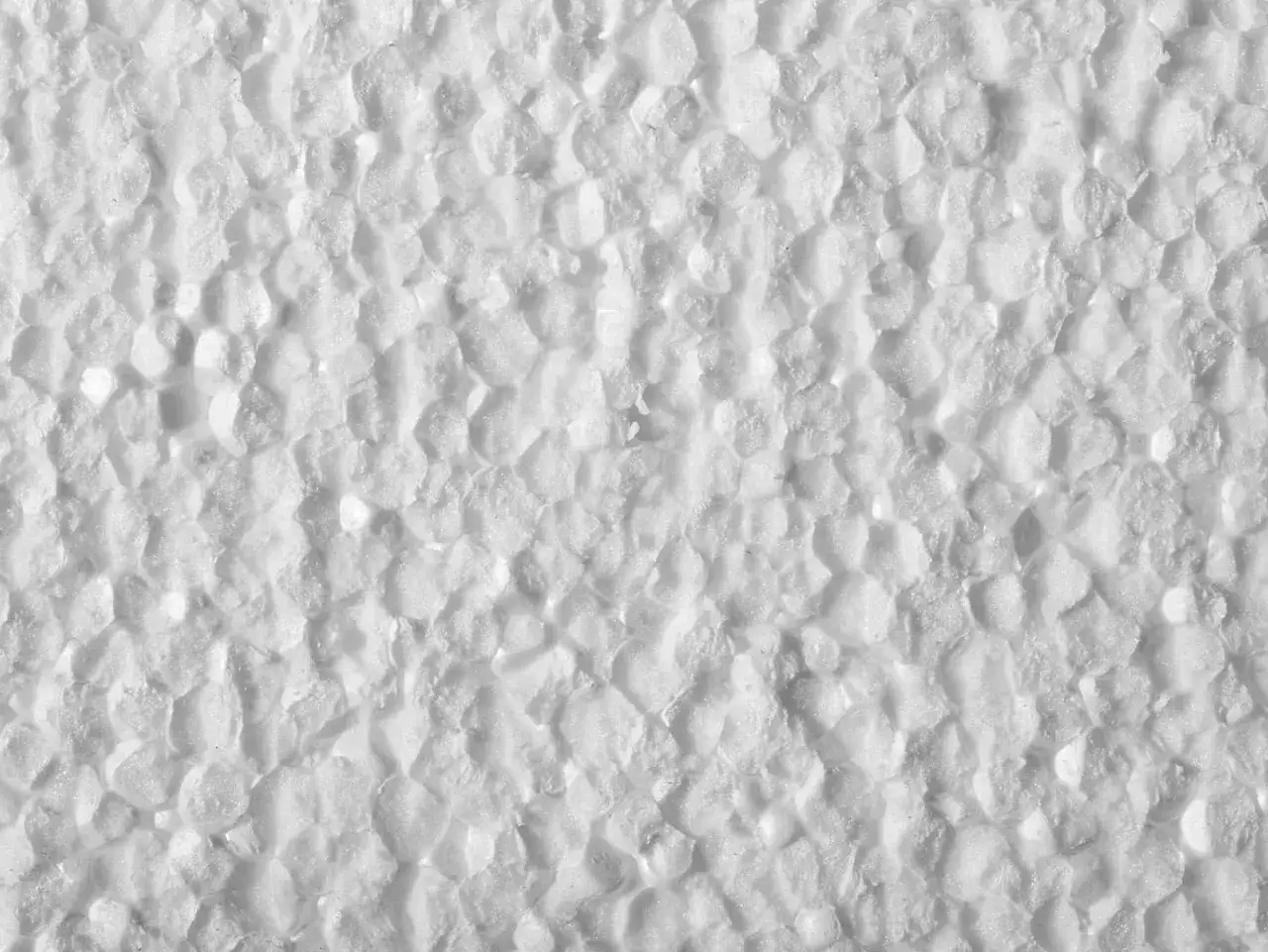 Tekstura białego styropianu, przypominająca małe, nieregularne kuleczki. Idealny materiał na izolację domu ze styropianu.