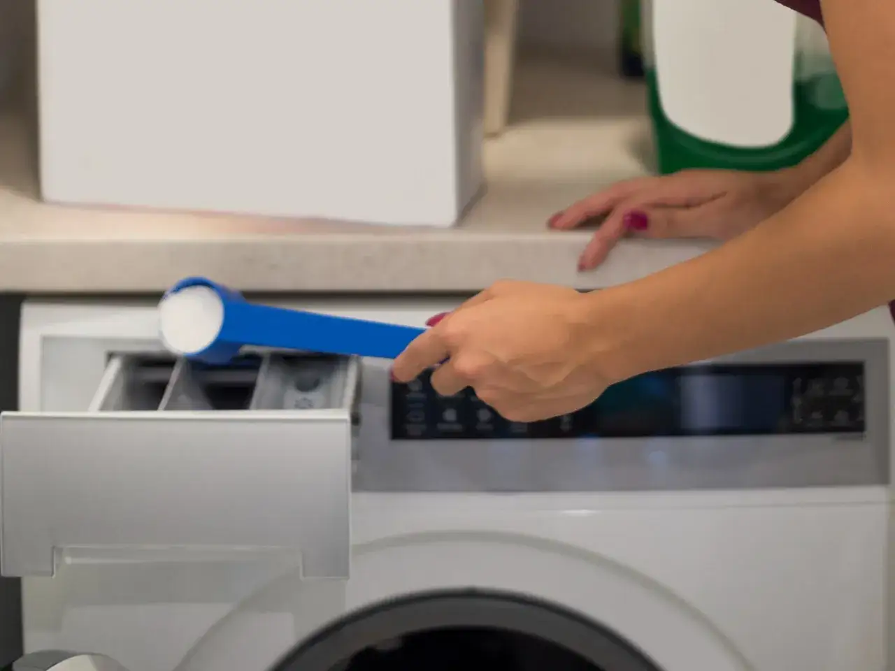 Kobieta wsypuje proszek do szuflady pralki, pokazując, jak wyczyścić pralkę.