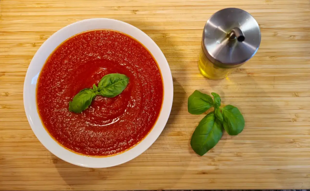 Miseczka z prawdziwym sosem do pizzy, ozdobiona listkami bazylii, obok buteleczka oliwy.