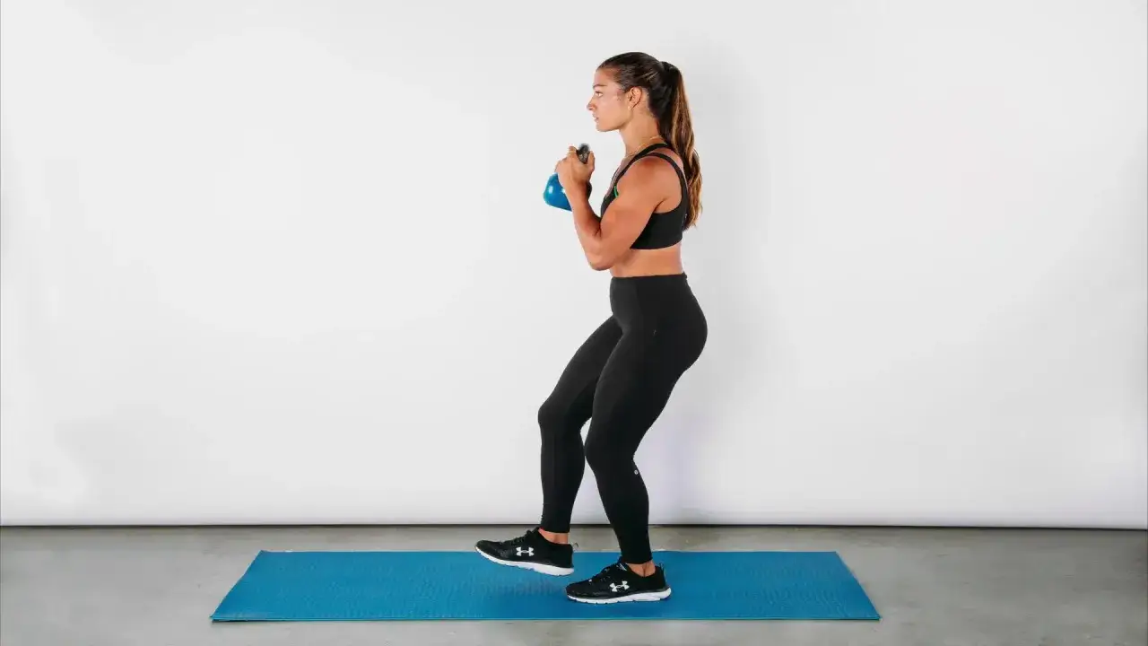 Kobieta wykonuje przysiad z kettlebell, ćwiczenie na jak wyszczuplić uda.