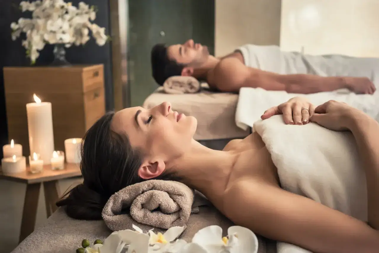 Para relaksujący dzień w spa dla dwojga. Para leży na stołach do masażu, otoczona świecami i kwiatami.