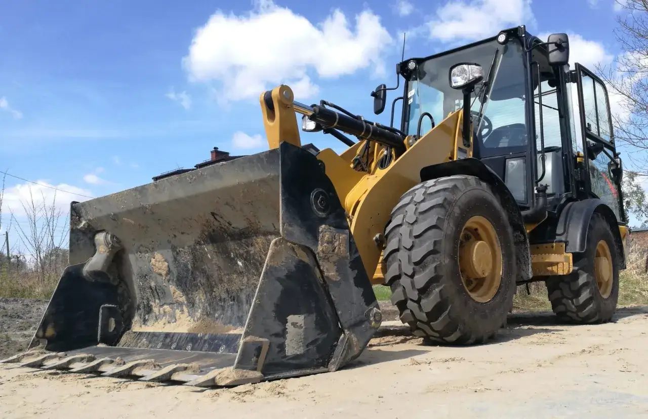 Żółta ładowarka stoi na piasku. Zastanawiasz się, ile zarabia operator koparki na godzinę?