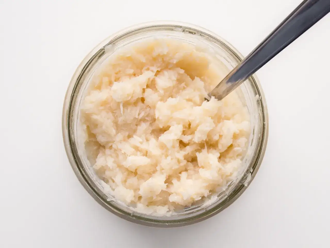 Słoik ze świeżo startym chrzanem, gotowy do przygotowania domowego chrzanu. Łyżeczka zanurzona w chrzanie.