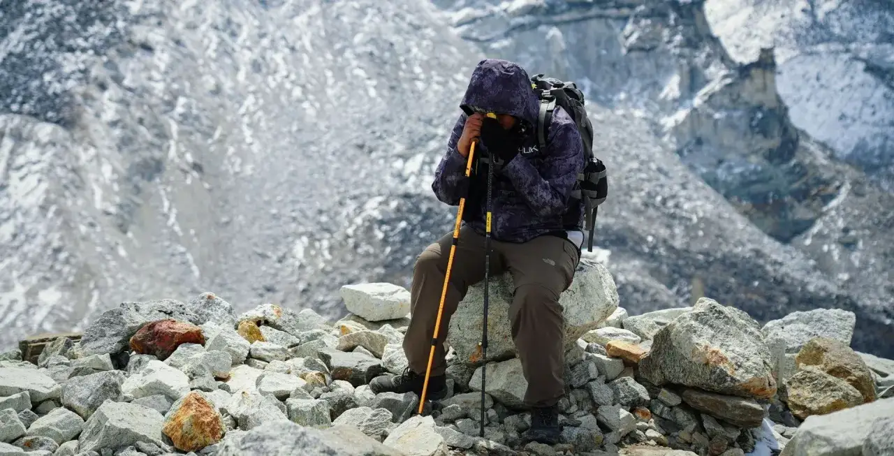 Wspinacz zmagający się z objawami **diuramid choroby wysokościowej** siedzi na kamieniach, opierając się o kijki.