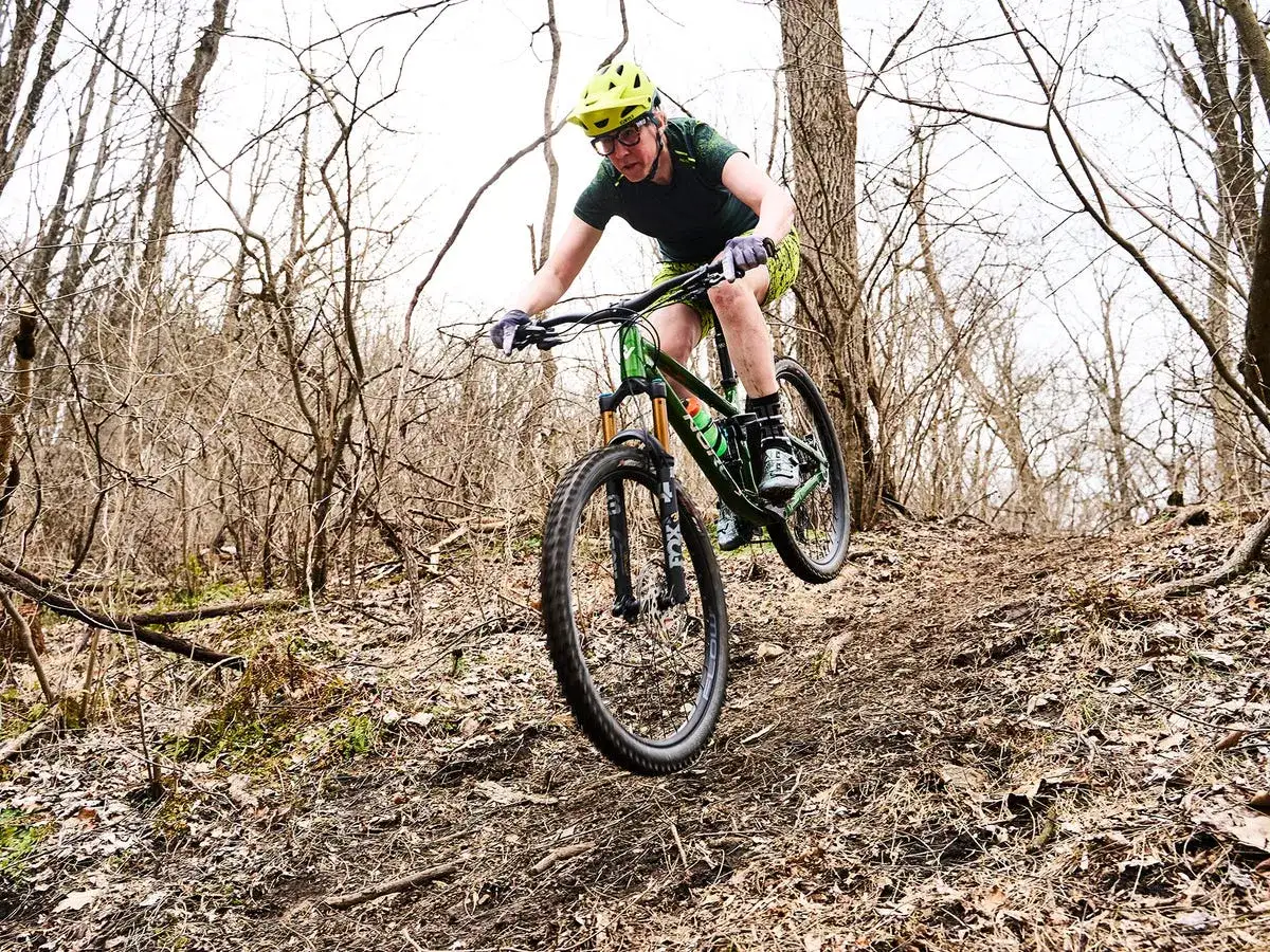 Kobieta na rowerze g&oacute;rskim 29 zjeżdża po leśnym szlaku.