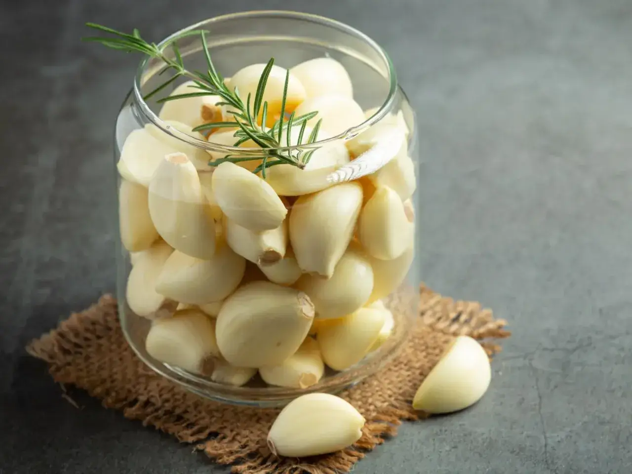 Słoik pełen ząbków czosnku z gałązką rozmarynu. Czy czosnek szkodzi na wątrobę? Zależy od ilości!