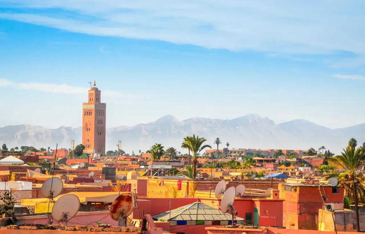 Widok na marrakesz atrakcje: minaret Koutoubia i czerwone dachy medyny na tle g&oacute;r Atlas.