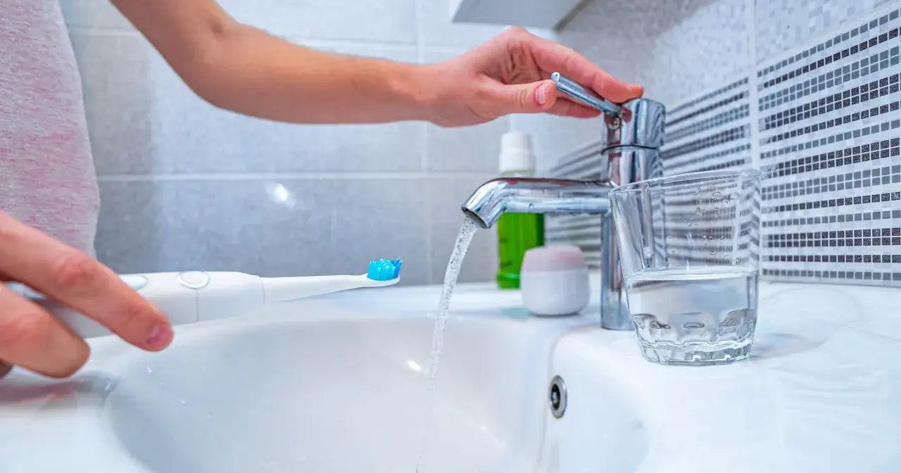 Ręka odkręca kran, by zmoczyć szczoteczkę. Dowiedz się, jak długo myć zęby, by były zdrowe.