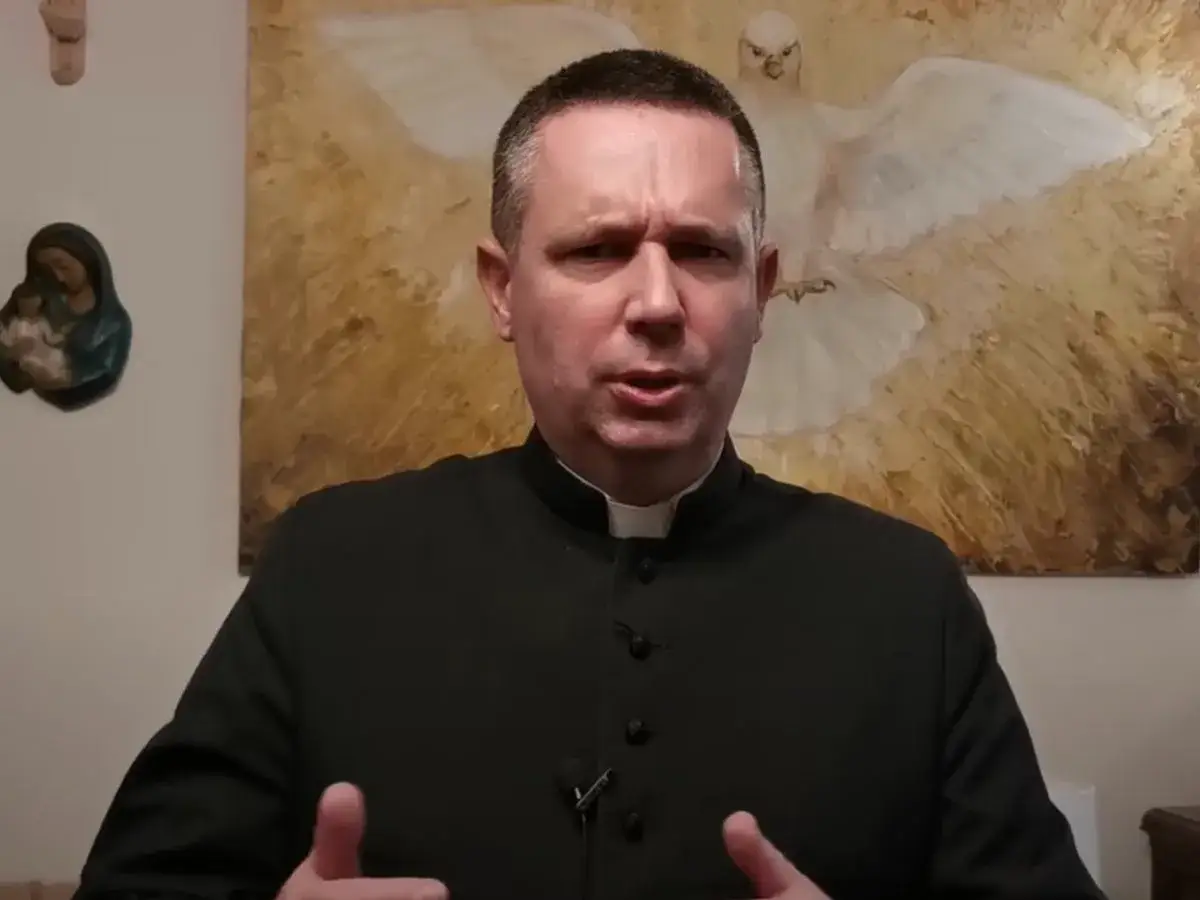 Duchowny w czarnej sutannie, z obrazem Ducha Świętego za plecami, wyjaśnia, co to znaczy pastor.