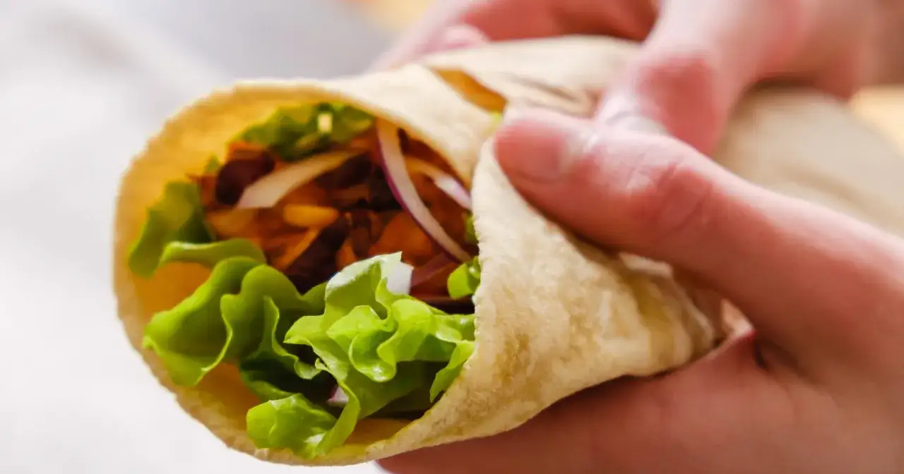 Ręce trzymają tortillę z sałatą, cebulą i mięsem. Czy tortilla jest tucząca? Zależy od nadzienia!